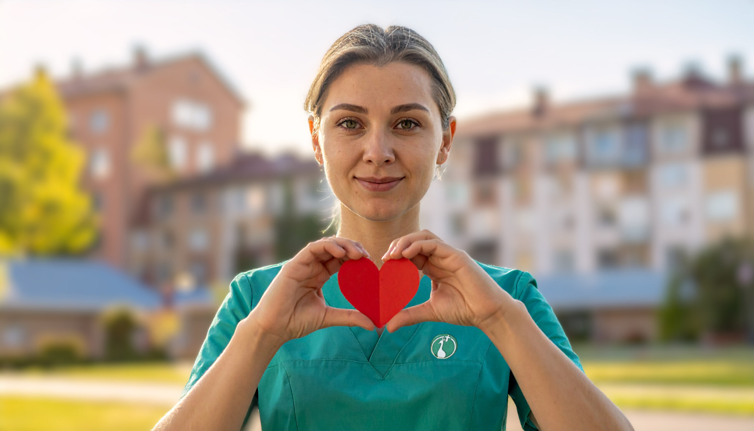 Auszubildende steht im Garten und hält ein Papierherz in beiden Händen