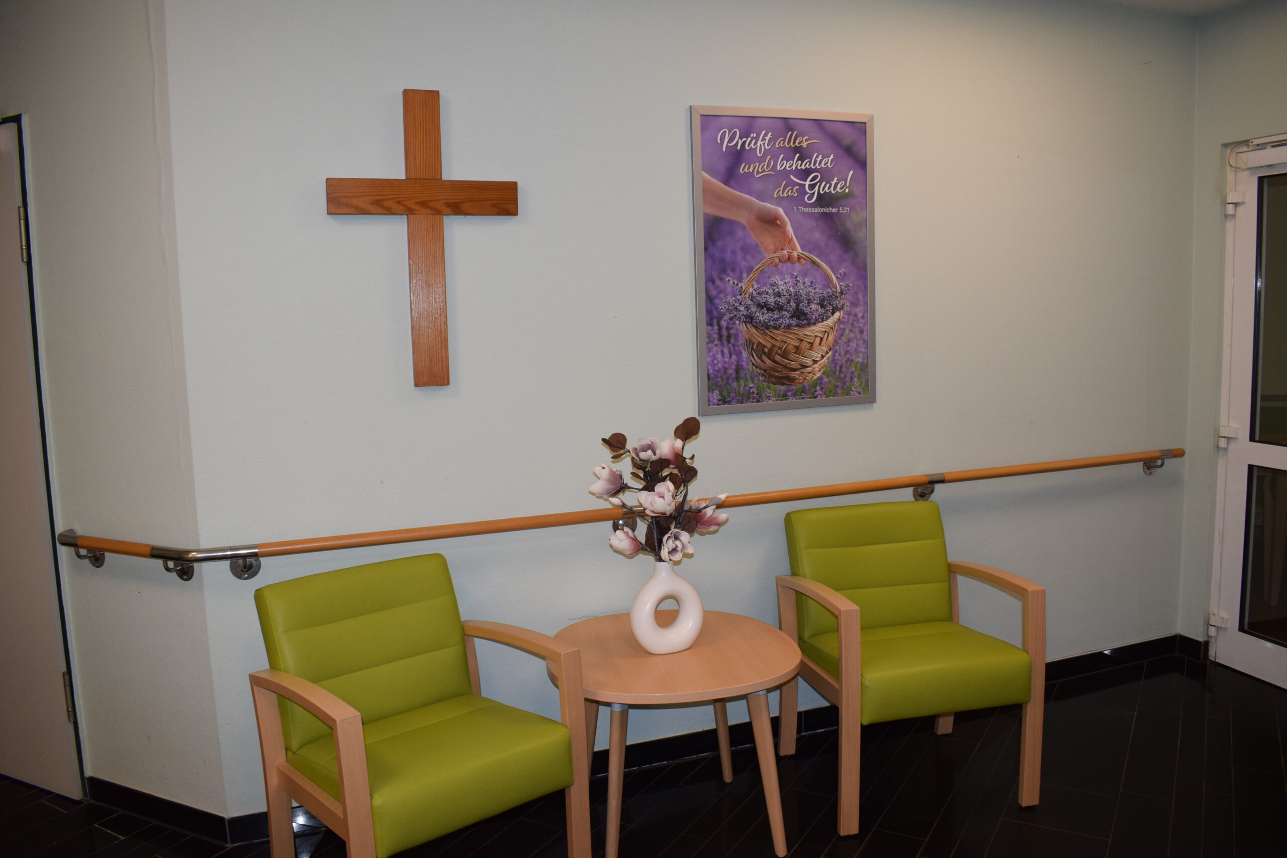 Im Eingangsbereich stehen zwei Stühle mit einem kleinen Tischchen mit Vase und an der Wand hängt ein Bild sowie das Zeichen Gottes.