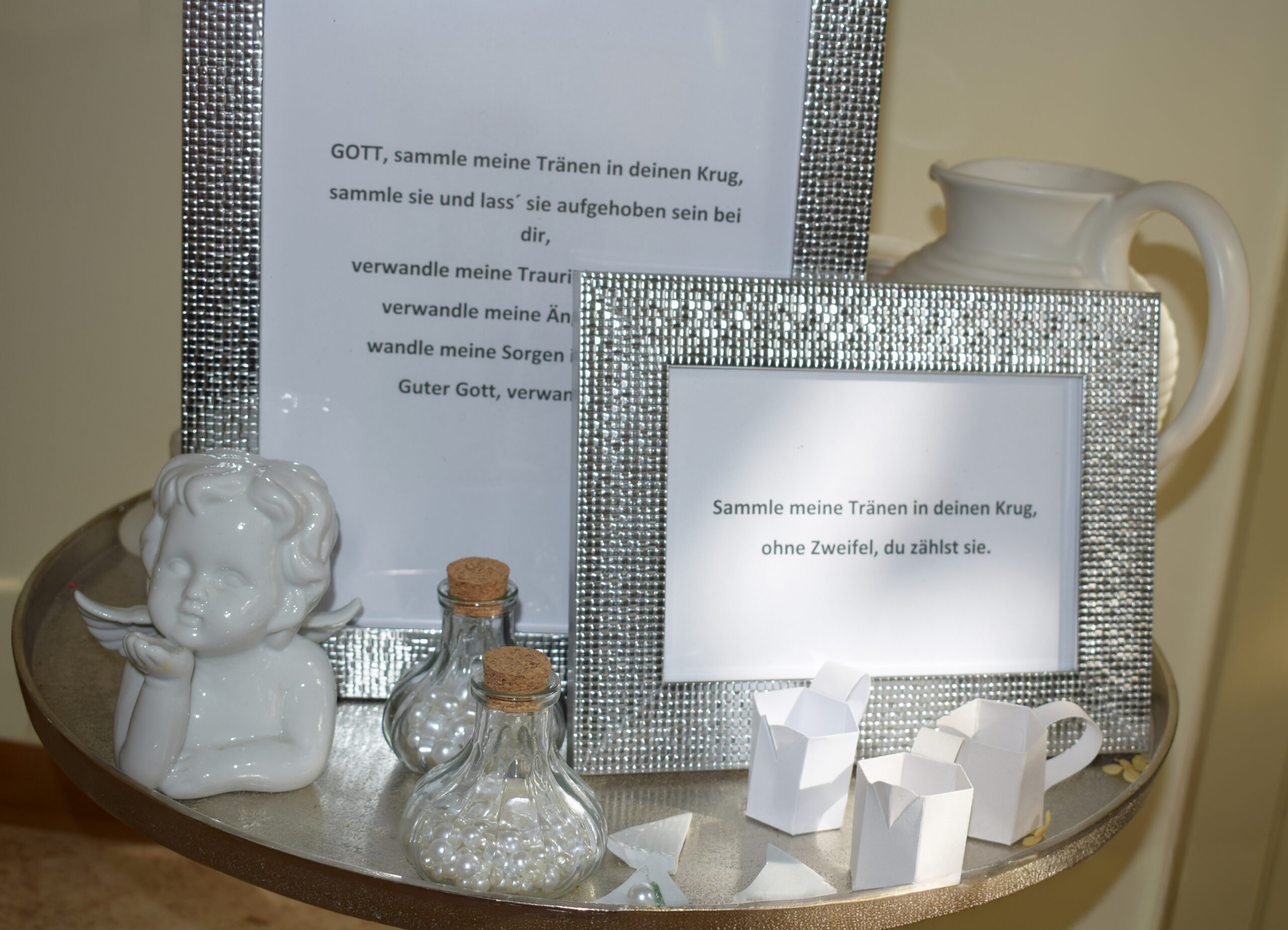Silberne Bilderrahmen mit Trosttext, Engel-Figur und kleine Glasfläschchen auf einem Tablett.